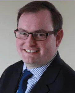 Andrew Blake Doggrell, smiling, in a dark suit and blue tie