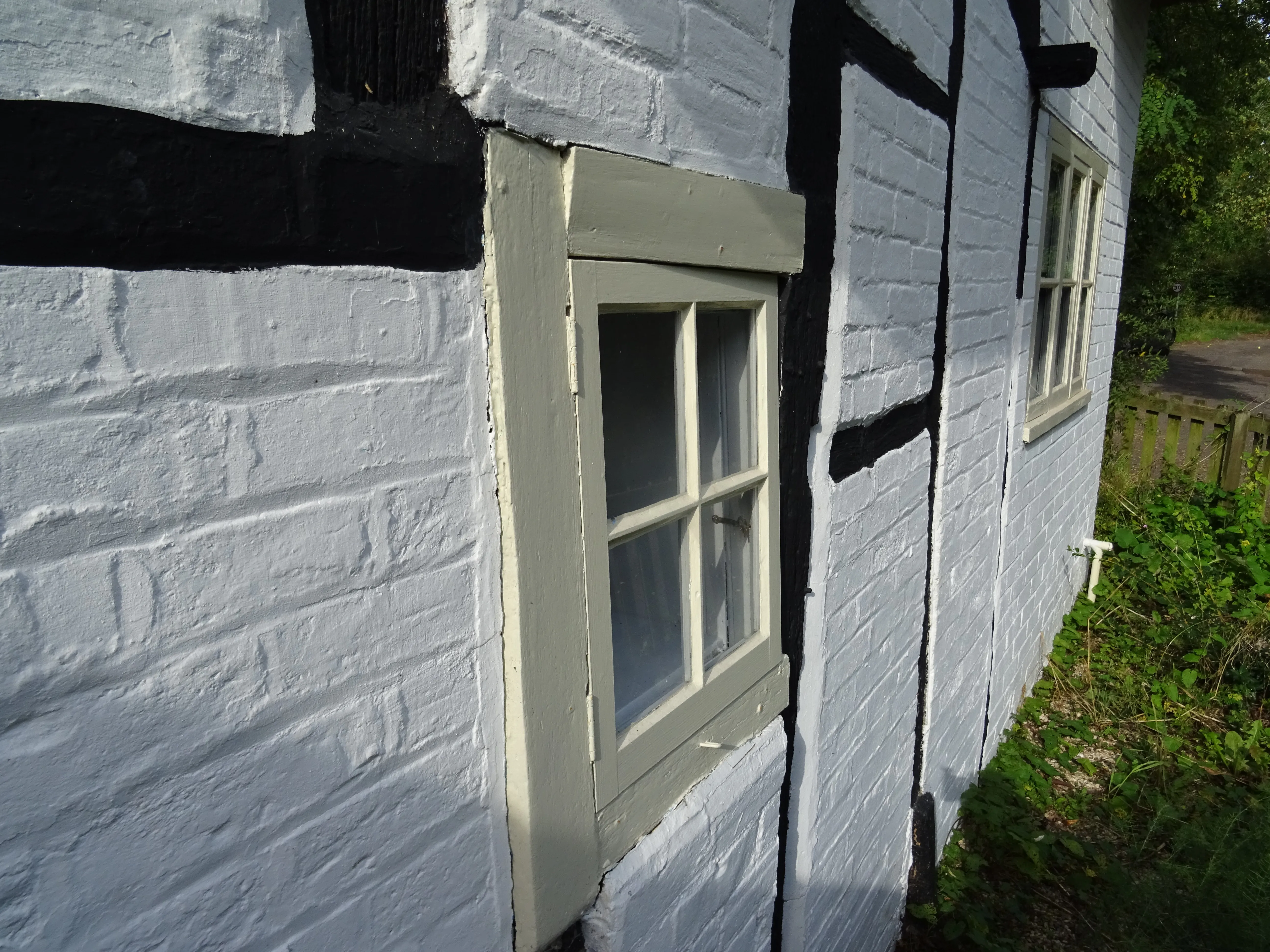The whitewashed wall of a cottage with black timber bands, bowing outwards beside a small window